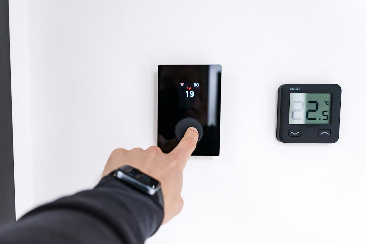 Finger adjusting a digital wall thermostat